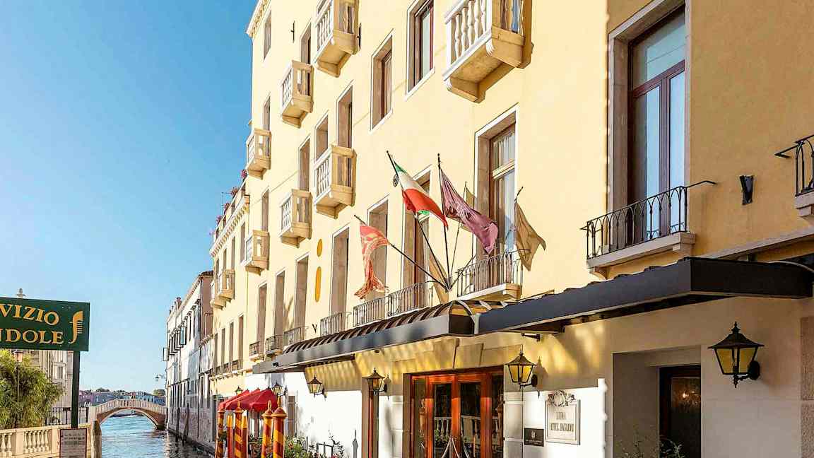 En gul byggnad med balkonger längs en kanal, med en gångbro i bakgrunden. (AI-genererad text)