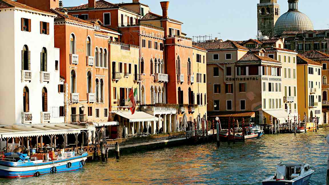 En bild av en kanal i Venedig med färgglada byggnader, båtar och en kupolformig kyrka i bakgrunden. (AI-genererad text)