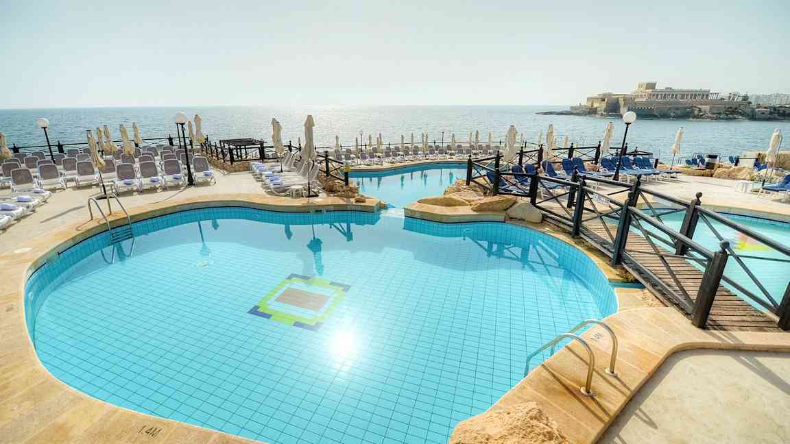 Bild av en utomhuspool vid stranden med solstolar och parasoll runt omkring. (AI-genererad text)