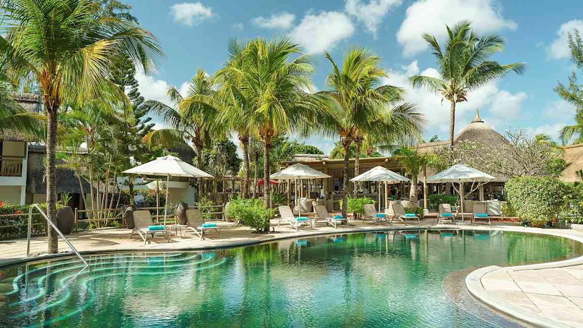 En exotisk pool omgiven av palmträd och solstolar under parasoller. (AI-genererad text)