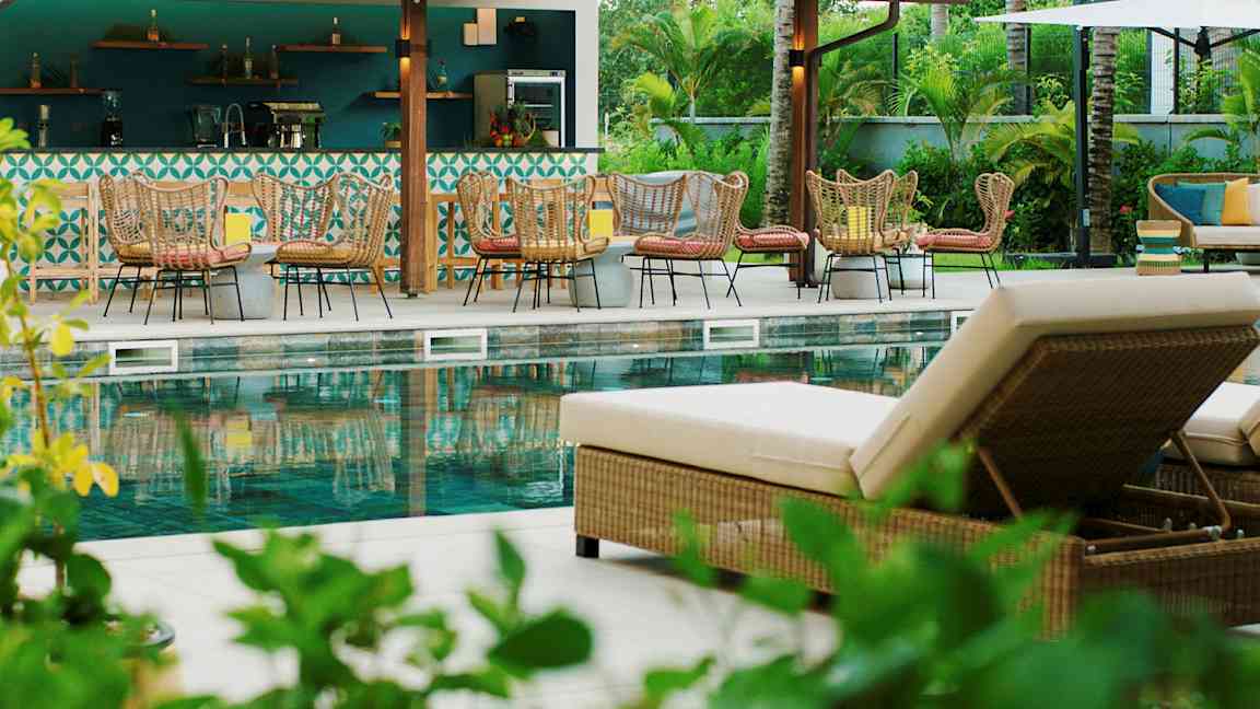 En utomhuspool med solstolar och sittgrupper vid en bar. (AI-genererad text)