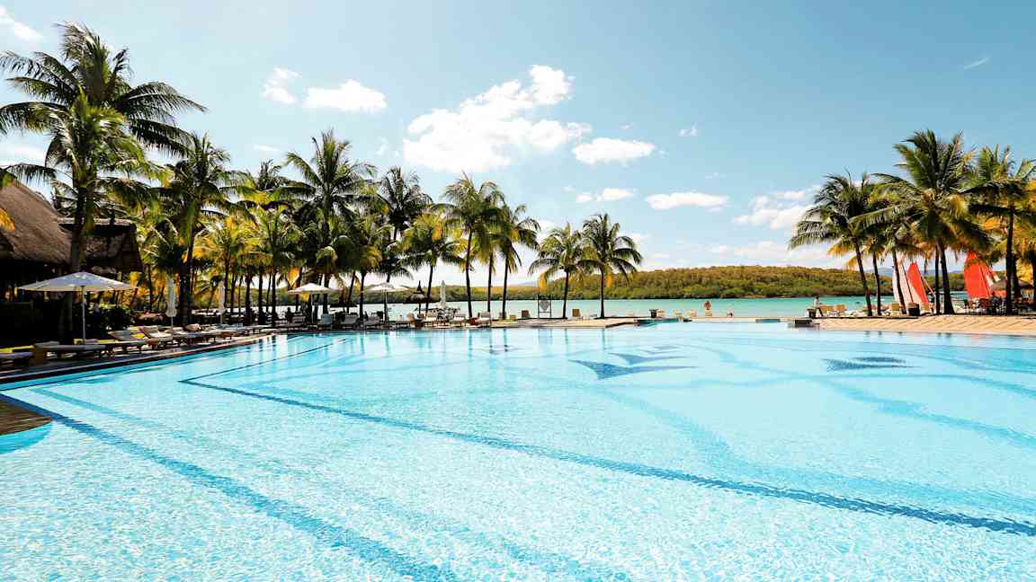 Stor pool vid havet omgiven av palmer. (AI-genererad text)