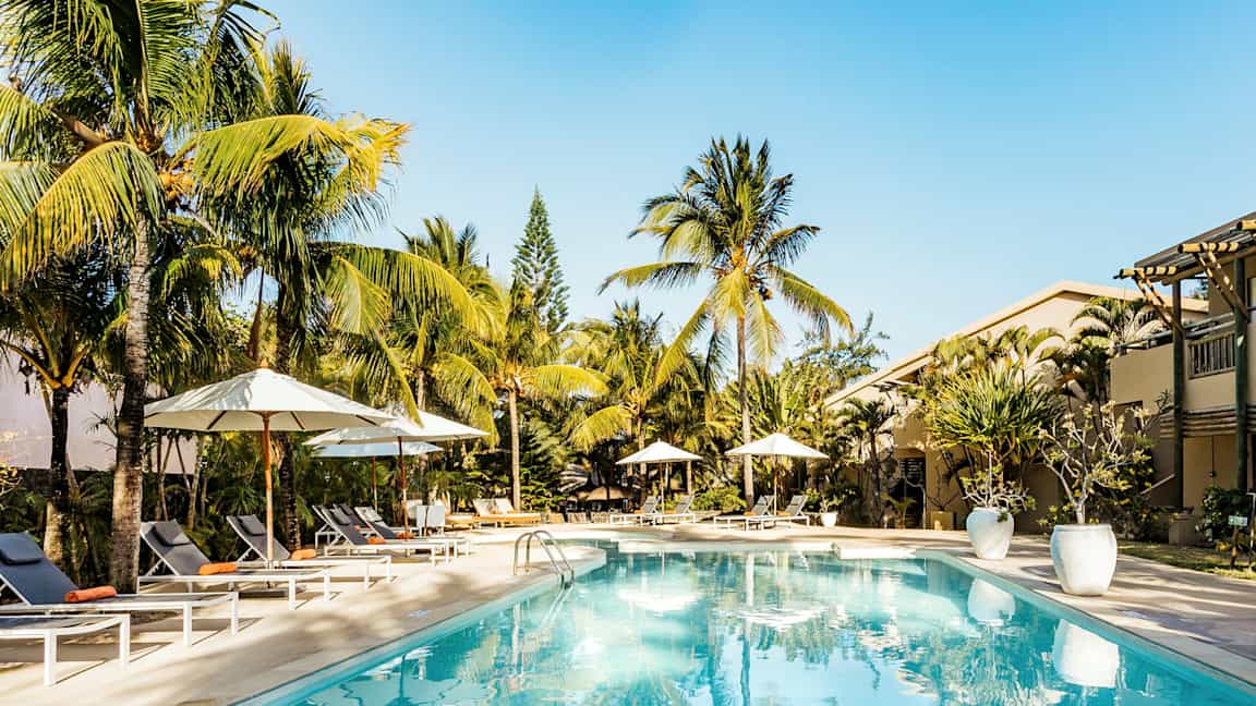 Poolområde med solstolar och parasoller, omgiven av palmer. (AI-genererad text)
