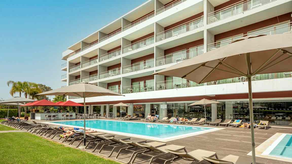 Hotellbyggnad med pool och solstolar. (AI-genererad text)