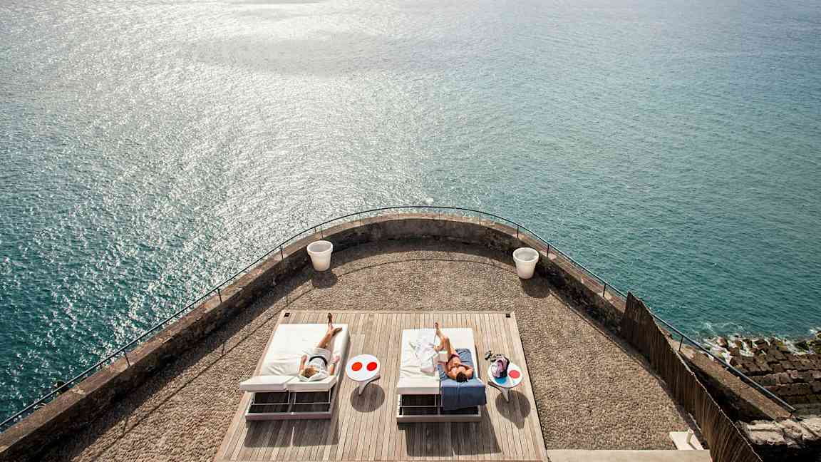 En terrass med två solstolar och havet i bakgrunden. (AI-genererad text)