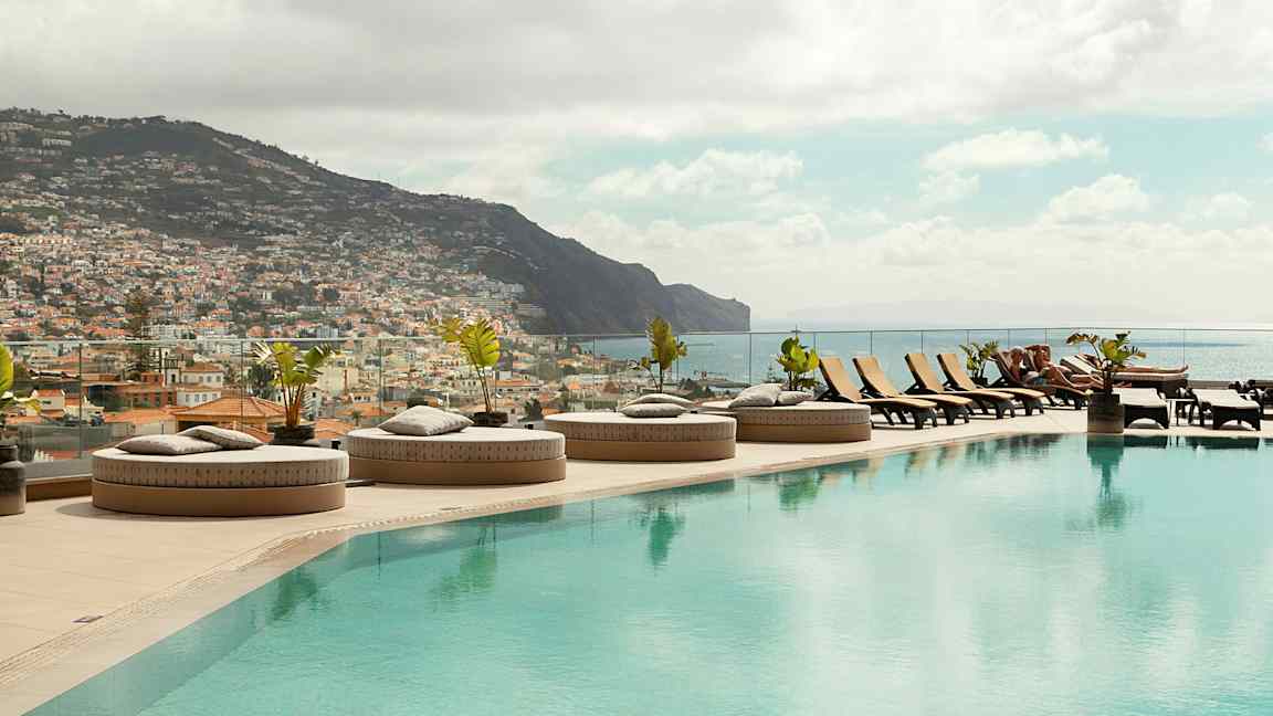 En infinitypool med solstolar och utsikt över en stad och berg. (AI-genererad text)