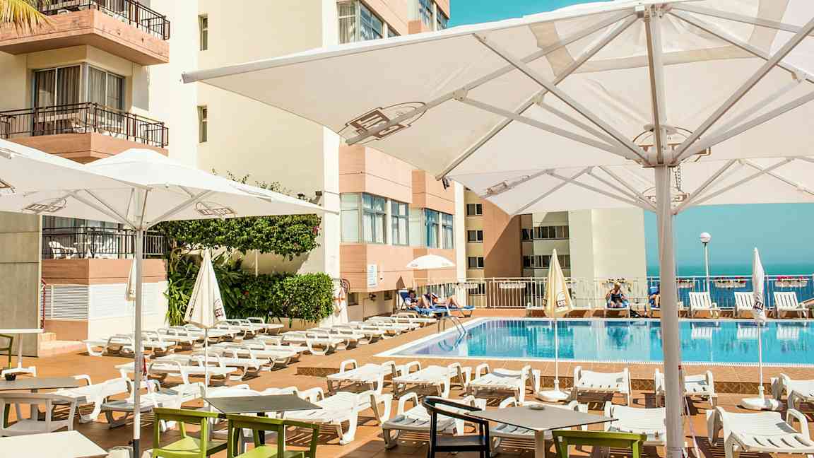 Utomhuspoolområde med solstolar och parasoller vid ett hotell. (AI-genererad text)