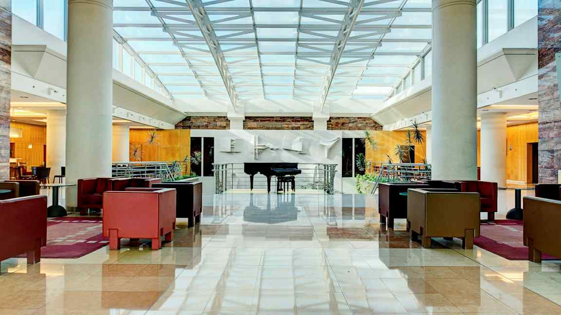 Ljus och rymlig hotellobby med sittgrupper och ett piano. (AI-genererad text)