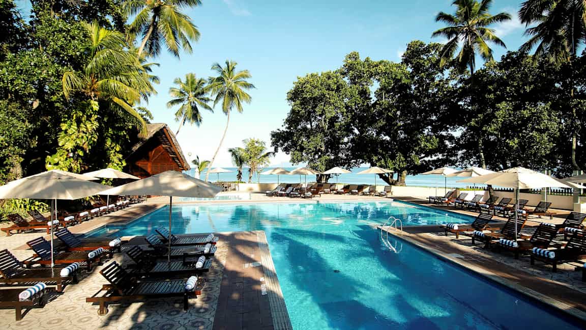 En pool med solstolar på ett tropiskt resortområde. (AI-genererad text)