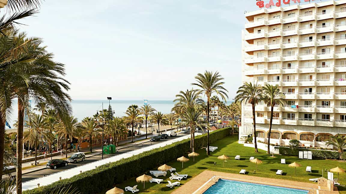 Bild av ett hotell med pool, palmer och utsikt över havet. (AI-genererad text)