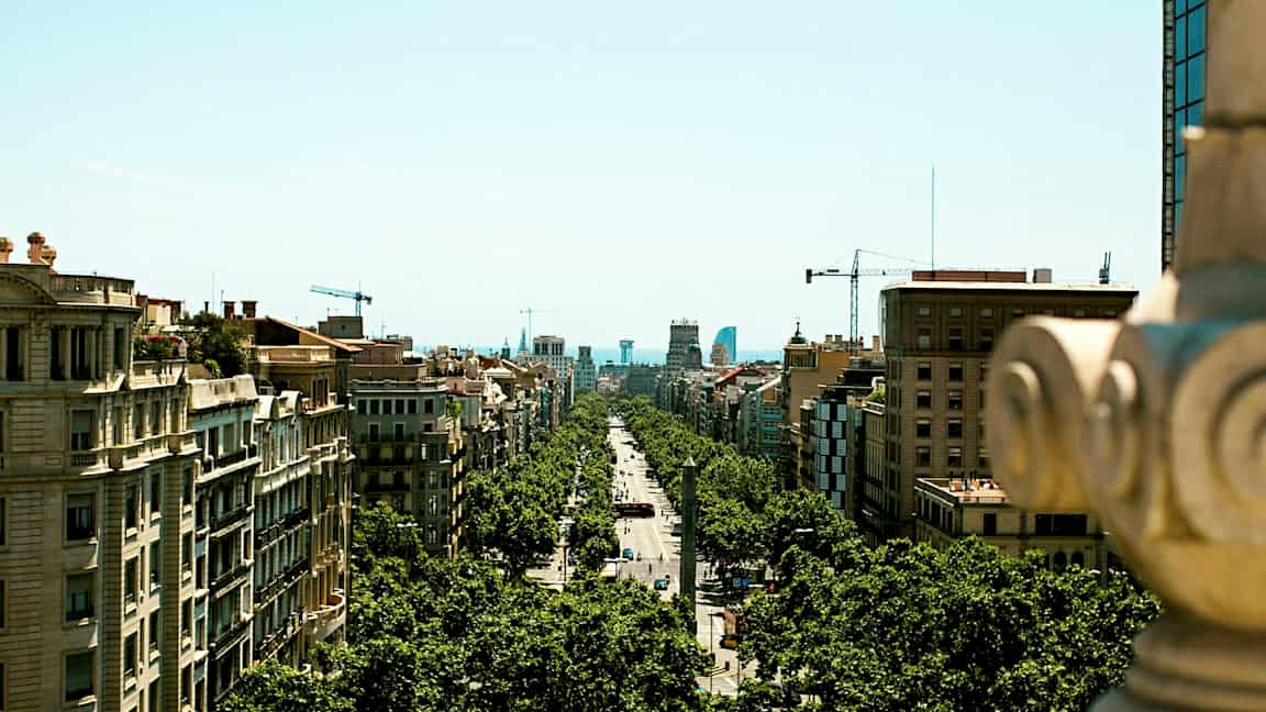 Vy över en stadsgata kantad av träd och omgiven av byggnader, fotograferad från en högre plats. (AI-genererad text)