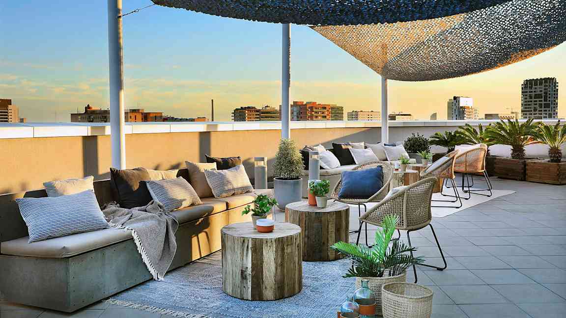 En takterrass med sittmöbler, bord och korgar dekorerade med växter och kuddar är avbildad. (AI-genererad text)