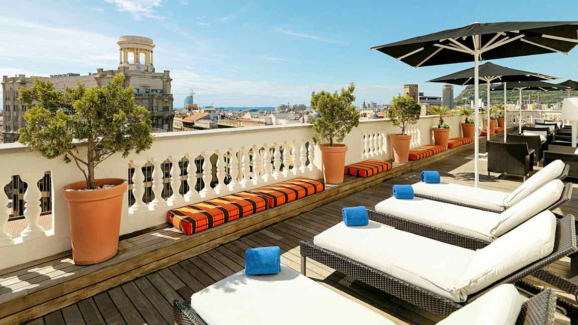 Utsikt över en terrass med solstolar och parasoller, med en stad och havet i bakgrunden. (AI-genererad text)