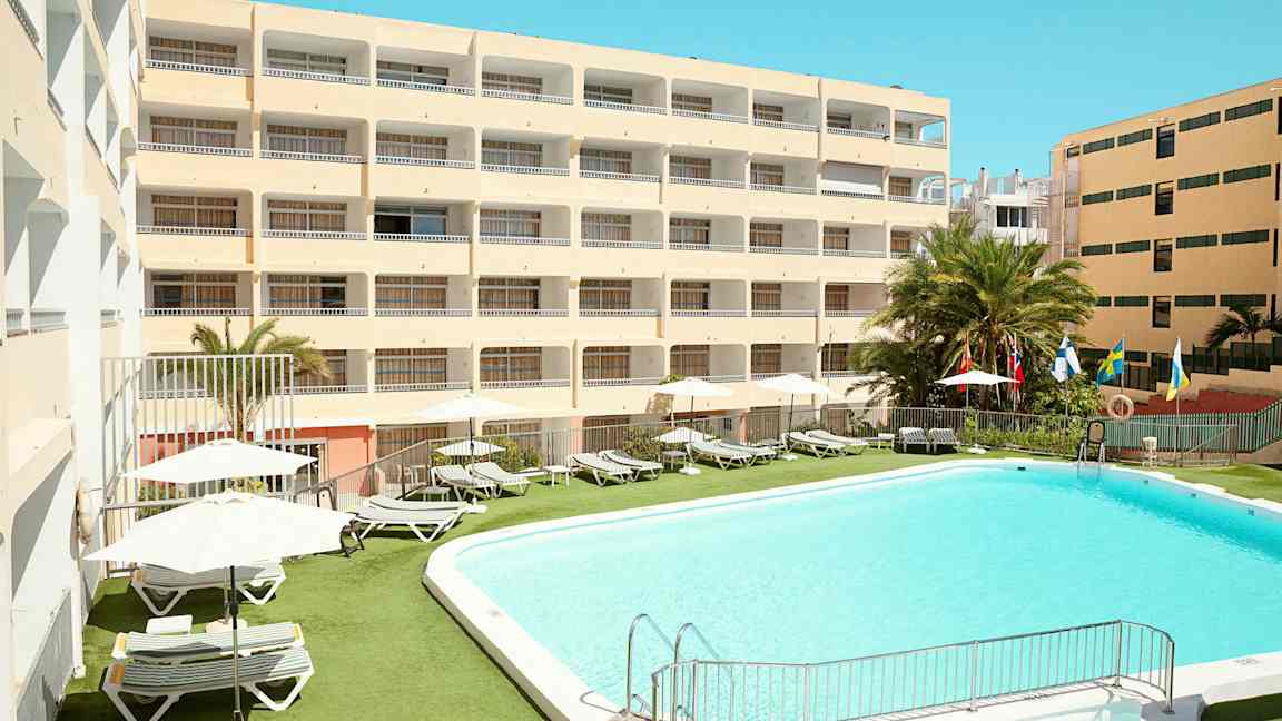 Hotellbyggnad med pool och solstolar utomhus. (AI-genererad text)