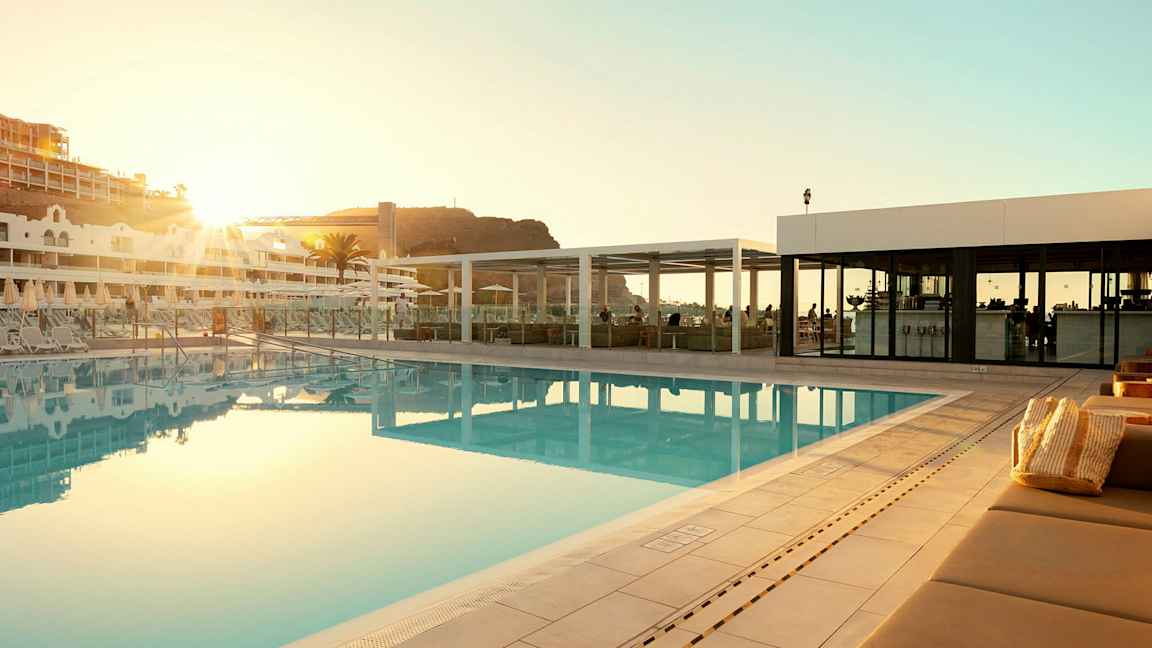 Utomhuspool vid ett hotell med solstolar och en byggnad i bakgrunden. (AI-genererad text)