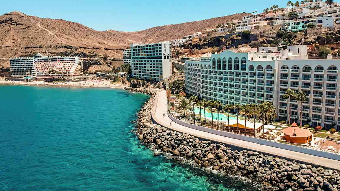 Hotell vid en kust med klippor, pool och palmer. (AI-genererad text)