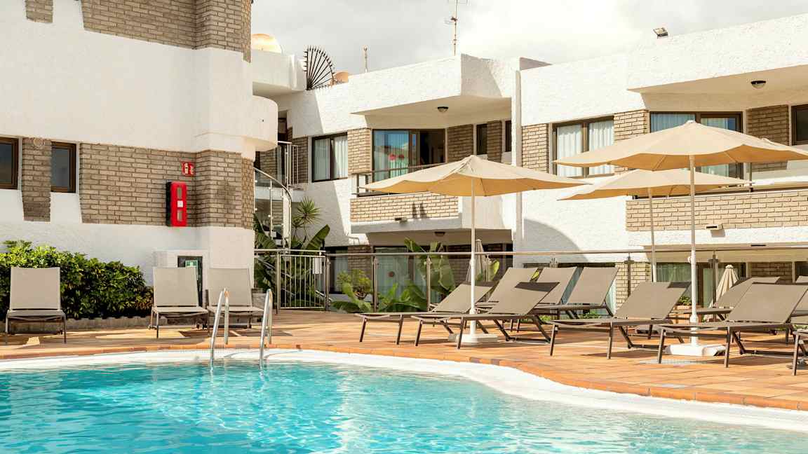 Utomhuspoolområde med solstolar och parasoller vid en byggnad. (AI-genererad text)