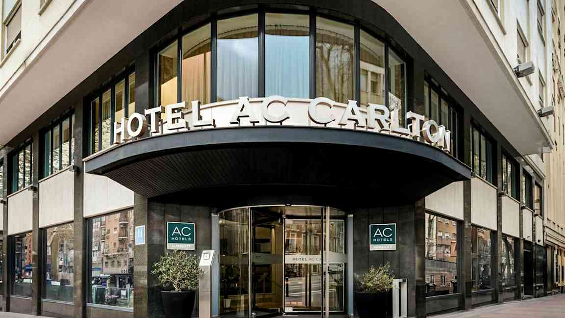 En hotellfasad med skylttexten "HOTEL AC CARLTON" synlig ovanför ingången. (AI-genererad text)