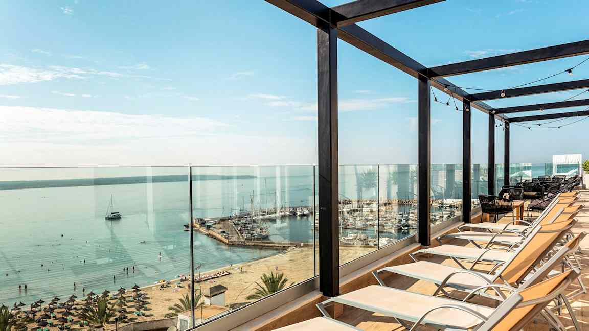 Solstolar uppställda framför glasräcke med utsikt över strand och hamn. (AI-genererad text)