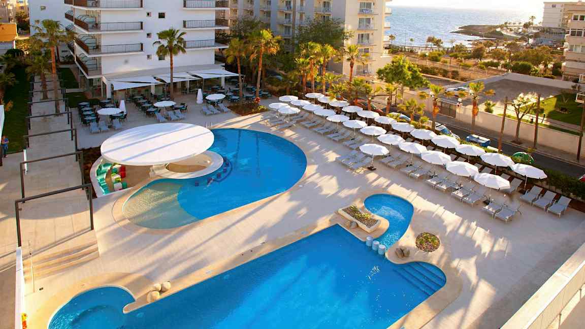 Hotellområde nära havet med pool, solstolar och parasoller. (AI-genererad text)