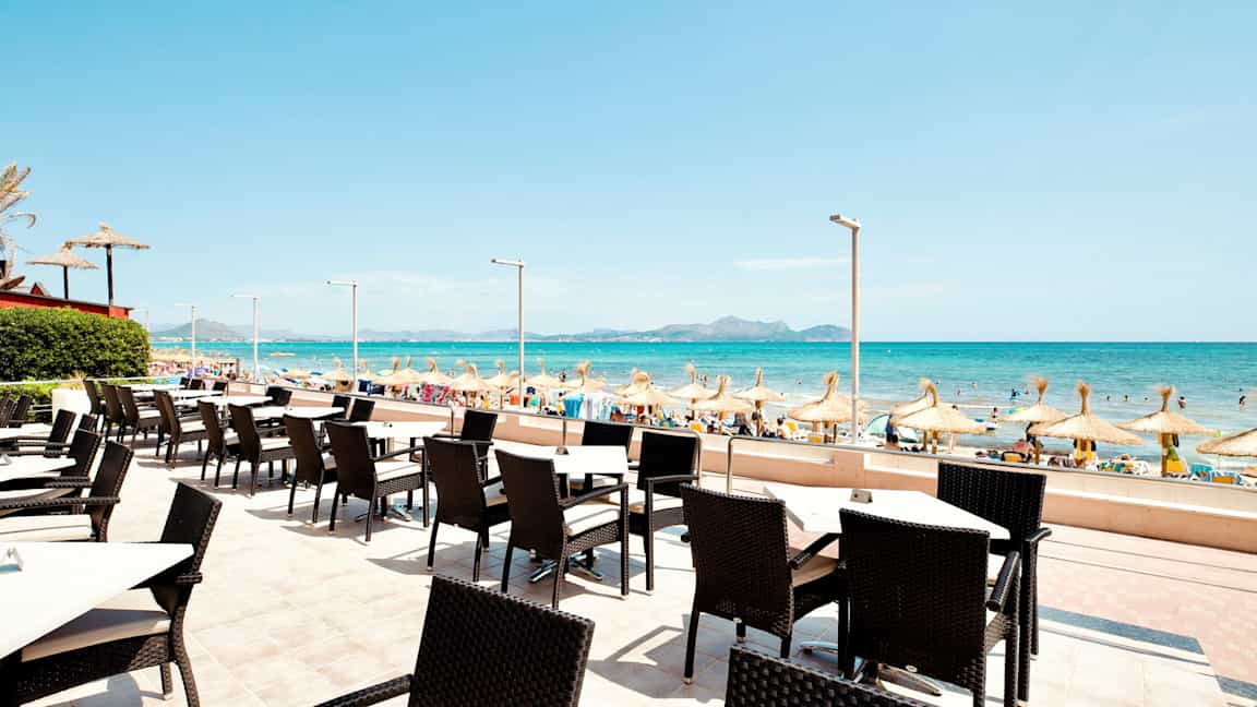 Uteservering med utsikt mot en sandstrand och havet med parasoller. (AI-genererad text)