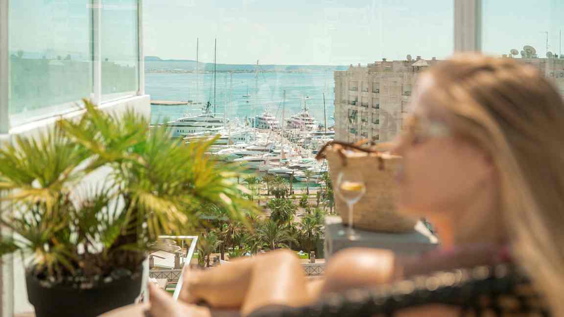 Utsikt mot båtar i en marina, med en glasbalkong och grönskande växter i förgrunden. (AI-genererad text)