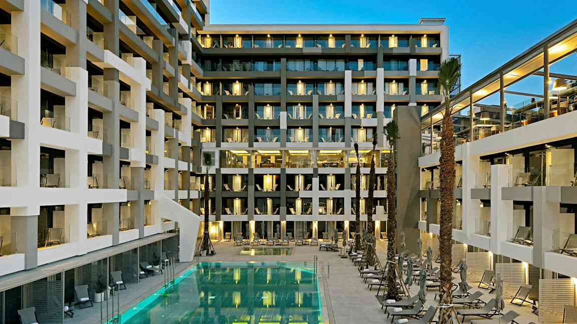En modern hotellbyggnad med balkonger och en upplyst pool omgiven av solstolar. (AI-genererad text)