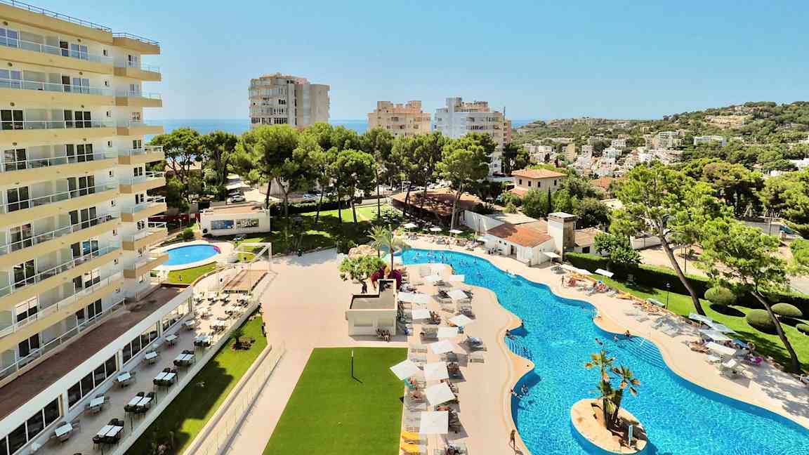 En hotellbyggnad bredvid en pool med solstolar och parasoller samt omgivande vegetation och utsikt över en stad. (AI-genererad text)