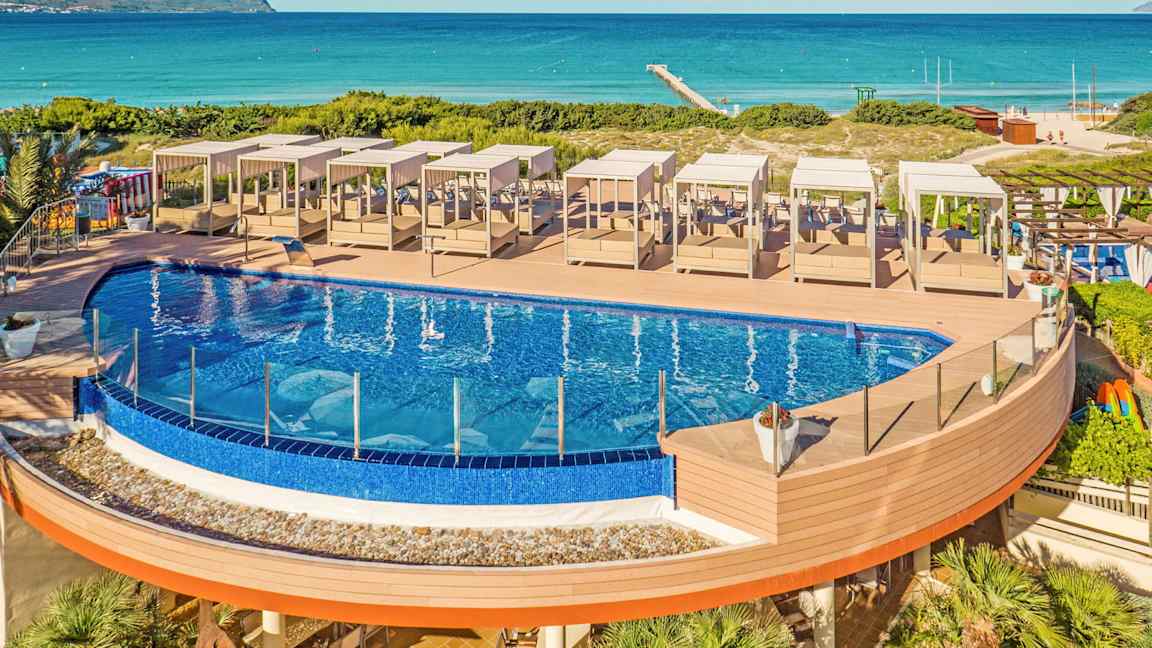 Utomhuspool med solstolar på ett trädäck nära stranden. (AI-genererad text)