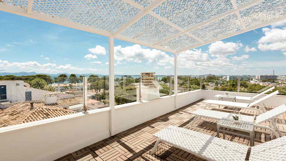 En takterrass med solstolar och ett bord. Terrassen har ett perforerat takskydd och glasräcke med utsikt över stad och hav. (AI-genererad text)