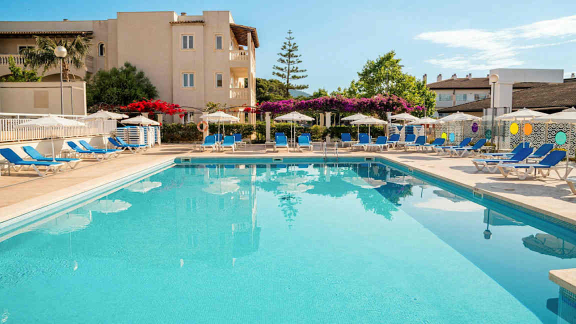 En utomhuspool omgiven av solstolar och parasoller vid ett hotell. (AI-genererad text)