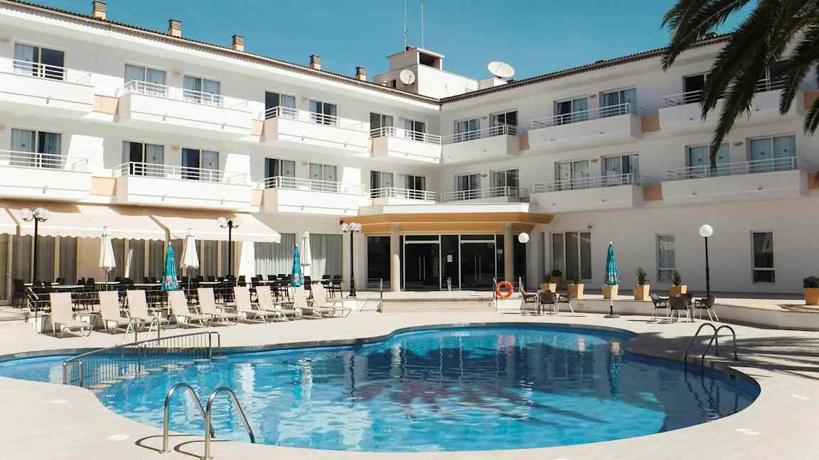 En pool framför en hotellanläggning med solstolar och parasoller. (AI-genererad text)