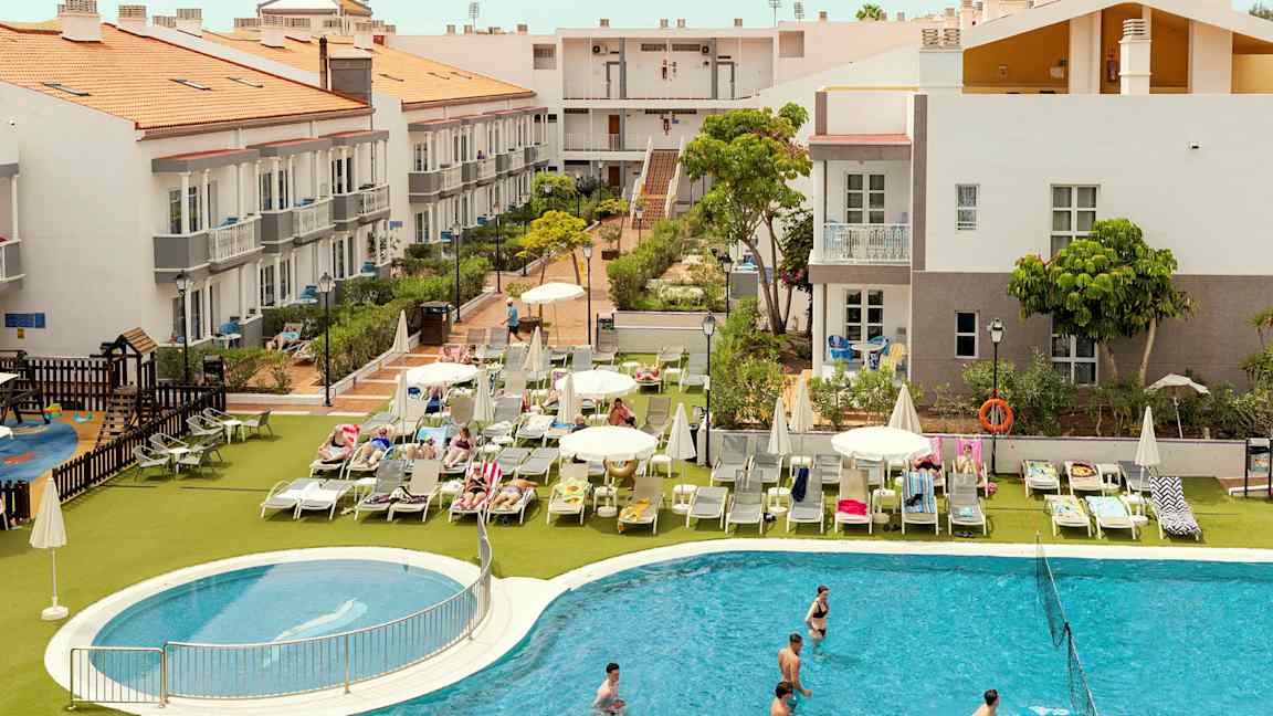 Hotellområde med byggnader, solstolar och en pool. (AI-genererad text)