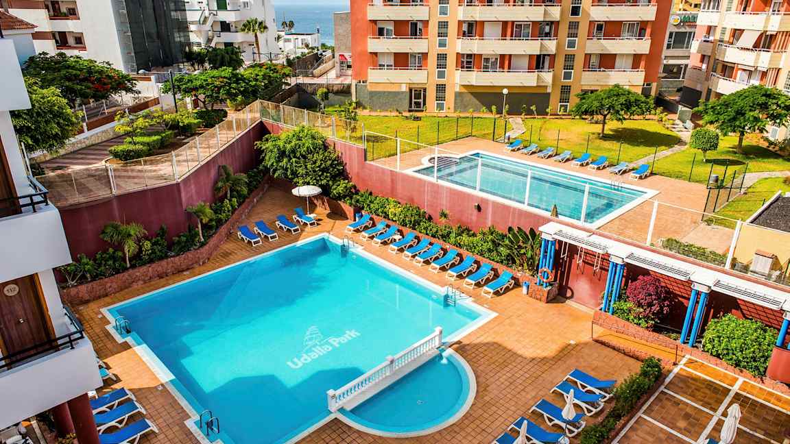 Ett hotellområde med två pooler, solsängar och omgivande byggnader. (AI-genererad text)