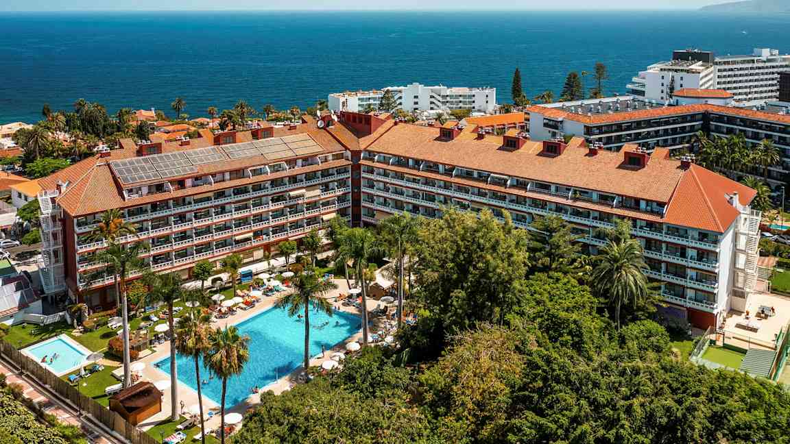 Flygfoto av ett hotellkomplex med pooler, palmer och havet i bakgrunden. (AI-genererad text)
