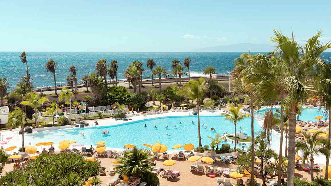 Poolområde med solstolar, parasoller och människor, med havet i bakgrunden. (AI-genererad text)