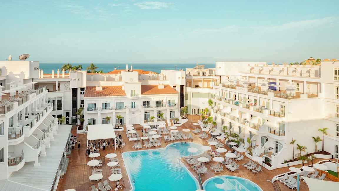 Vy över hotellområde med pool och solstolar, havet syns i bakgrunden. (AI-genererad text)