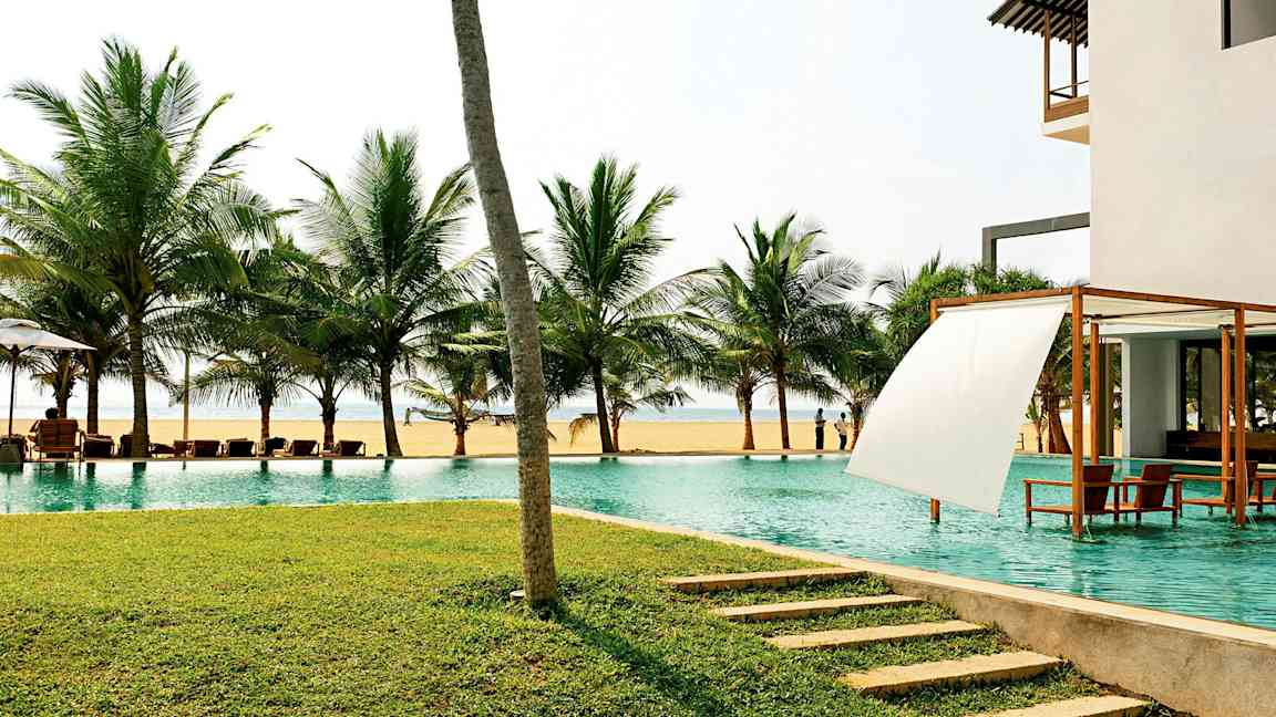 En pool vid havet med palmer i bakgrunden och en gräsmatta i förgrunden. (AI-genererad text)