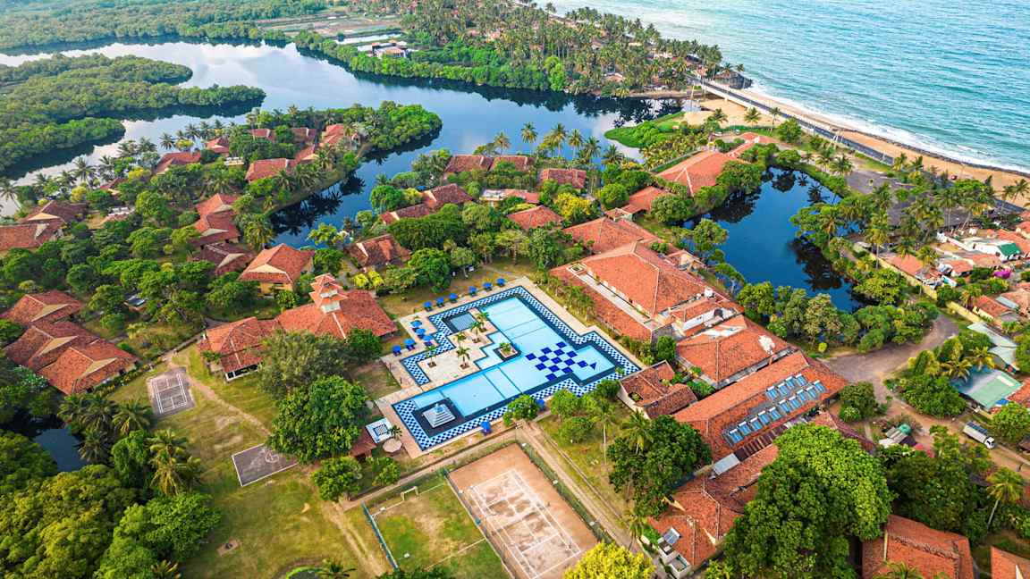 Luftfoto av en resort med terrakottafärgade tak, en stor pool och omgivande grönska. (AI-genererad text)