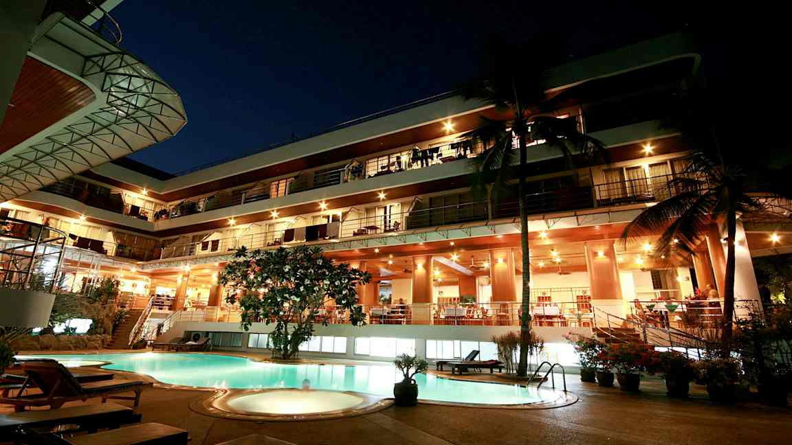 Kvällsvy av en byggnad med flera våningar, lysande fasad och en pool i förgrunden. (AI-genererad text)