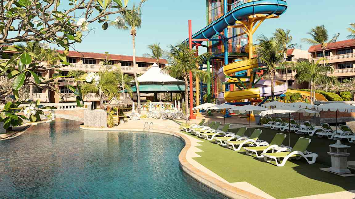 En pool vid ett hotell med en färgglad rutschkana och solstolar. (AI-genererad text)