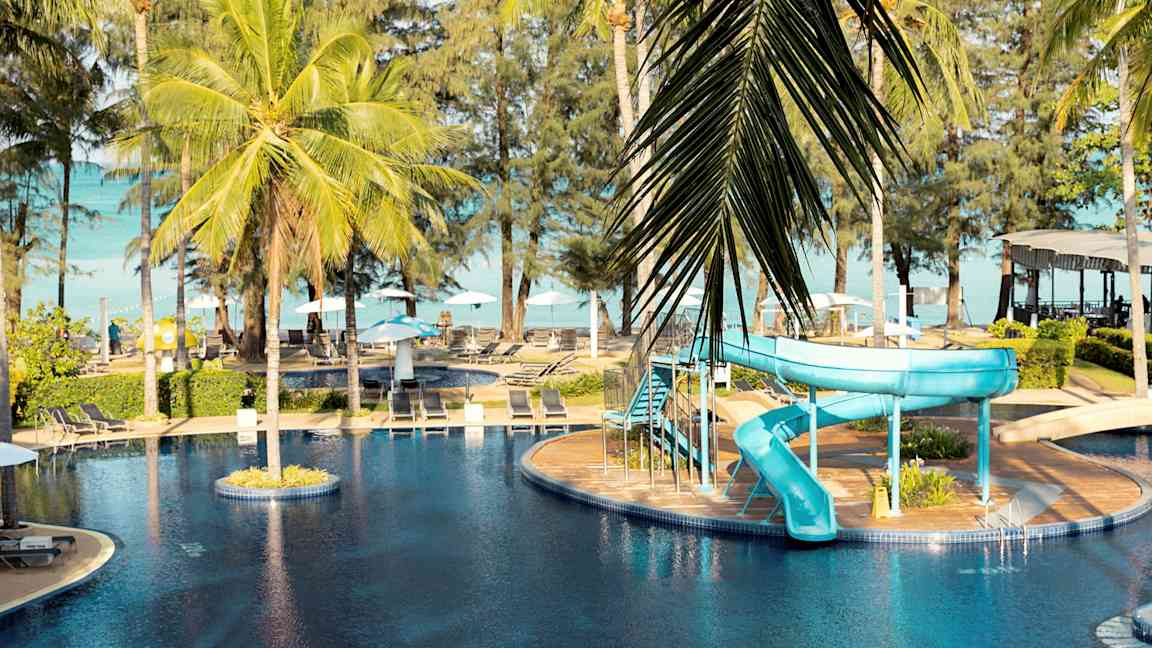 En utomhuspool med en blå vattenrutschkana och palmer runtom. (AI-genererad text)