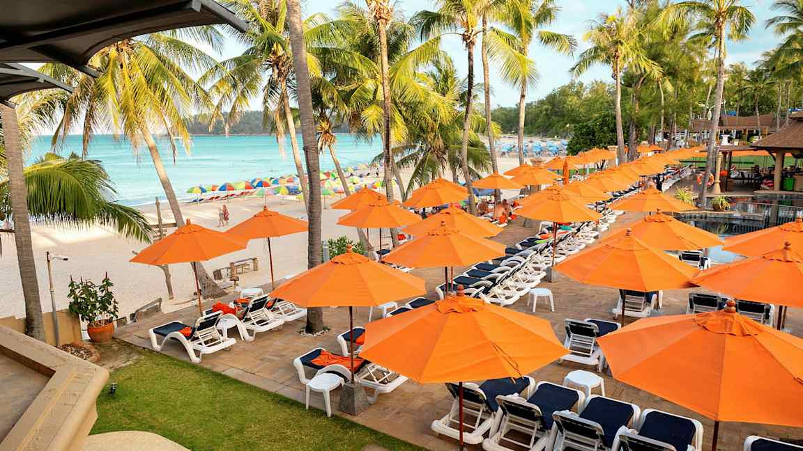 Solstolar och orange parasoll vid en strand med palmer. (AI-genererad text)