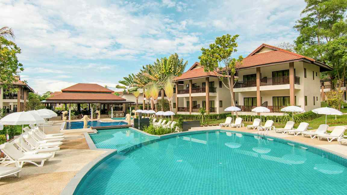Utsikt över poolområde med solstolar och parasoller framför hotellbyggnader. (AI-genererad text)