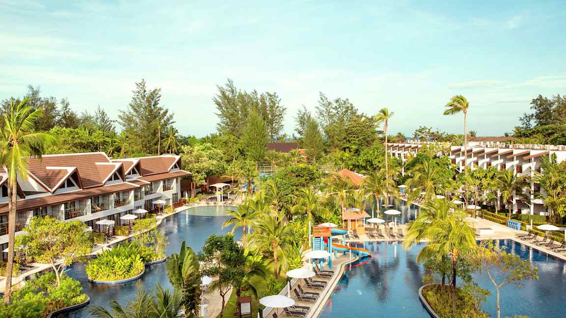 Hotellområde med en stor pool omgiven av palmer och byggnader. (AI-genererad text)