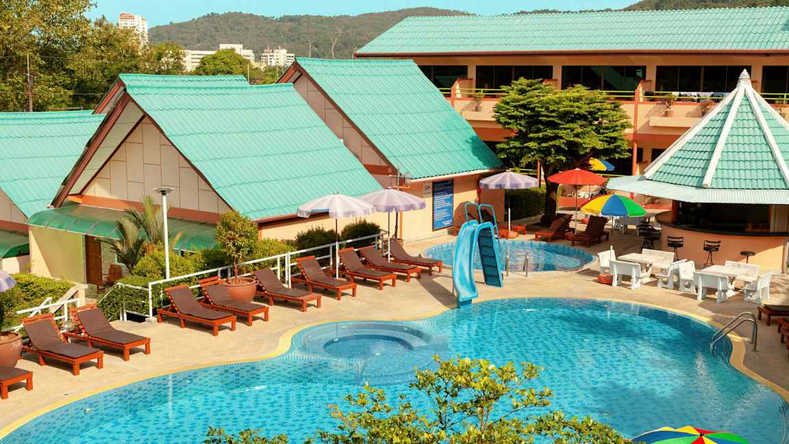 Utomhuspoolområde med solstolar, parasoller och byggnader med gröna tak. (AI-genererad text)