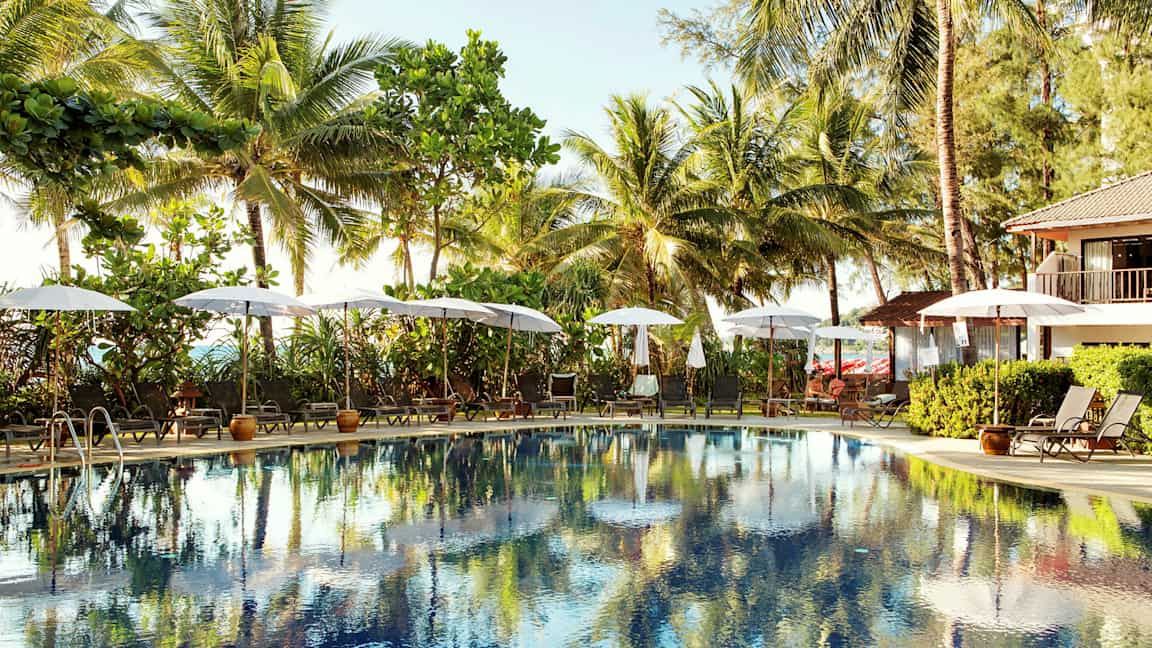 Utomhuspool omgiven av solstolar och parasoller, med palmer i bakgrunden. (AI-genererad text)