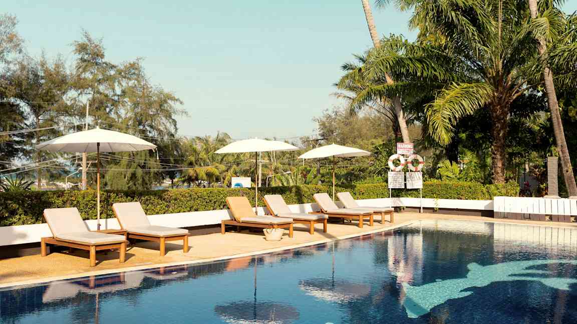 En utomhuspool med solsängar och parasoller. Tropiska träd i bakgrunden. (AI-genererad text)