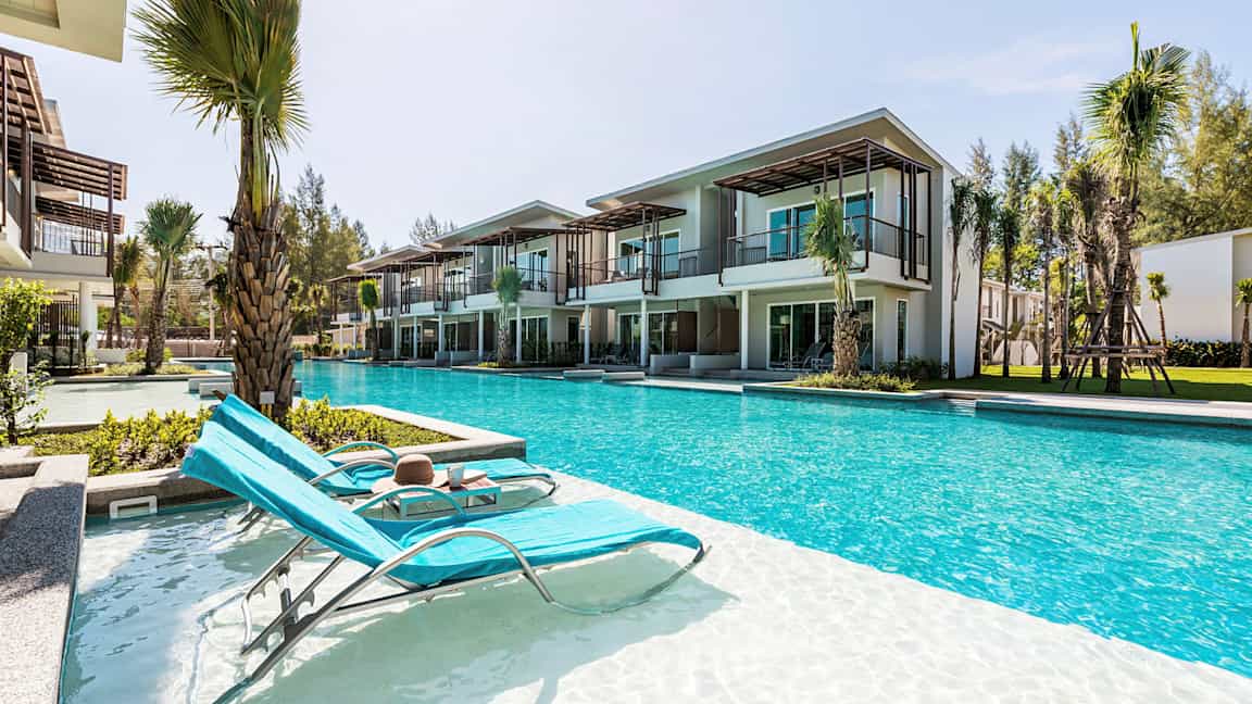 Bild av solstolar vid en pool framför moderna semesterboenden. (AI-genererad text)