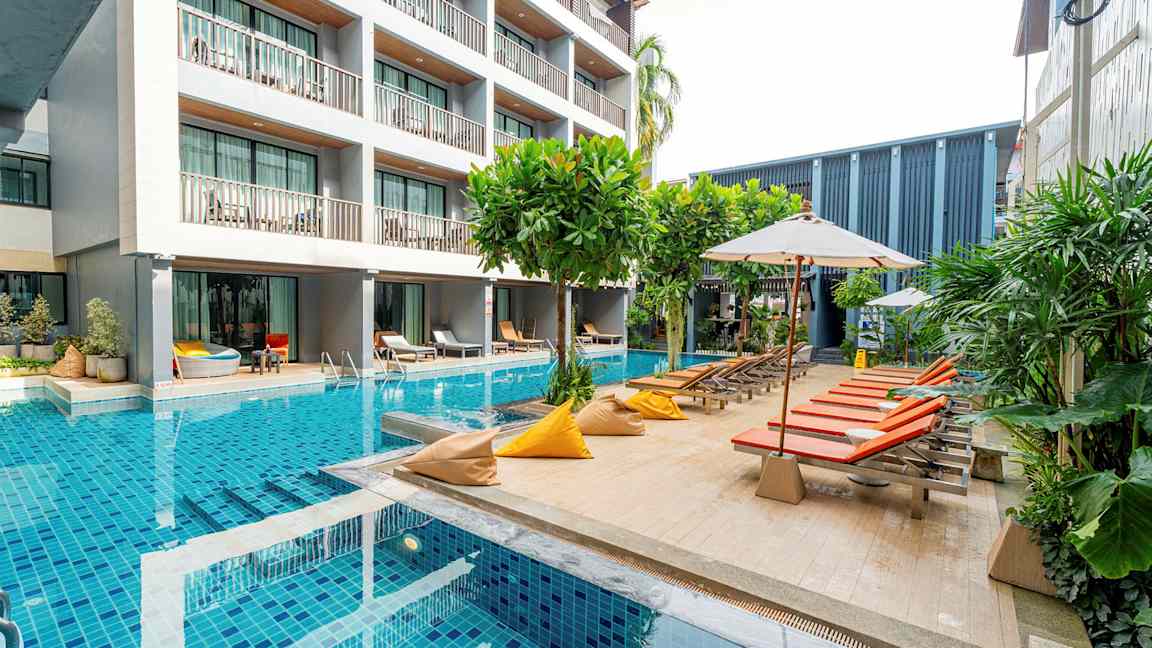 En modern hotellbyggnad intill en pool med solstolar och parasoller. (AI-genererad text)